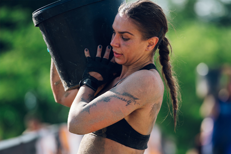 Mujer atlética llevando un saco de peso en una carrera de obstáculos