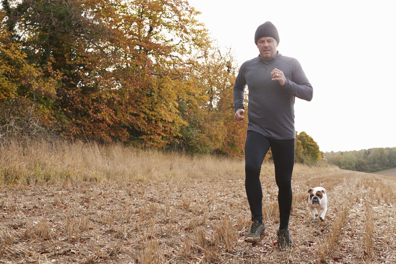 Un hombre con ropa de invierno corriendo por el bosque con su perro