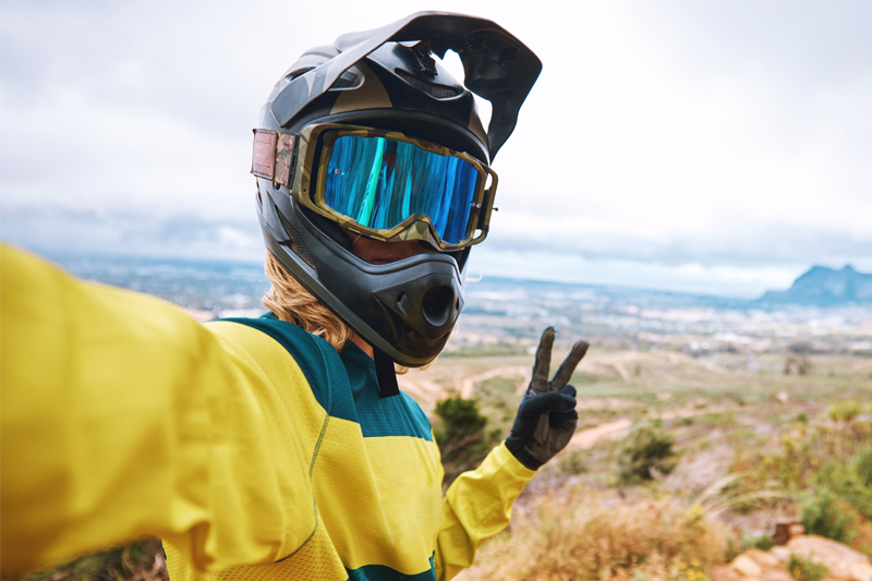Ciclista con casco y gafas de seguridad haciéndose un selfie antes de hacer un descenso con su bicicleta